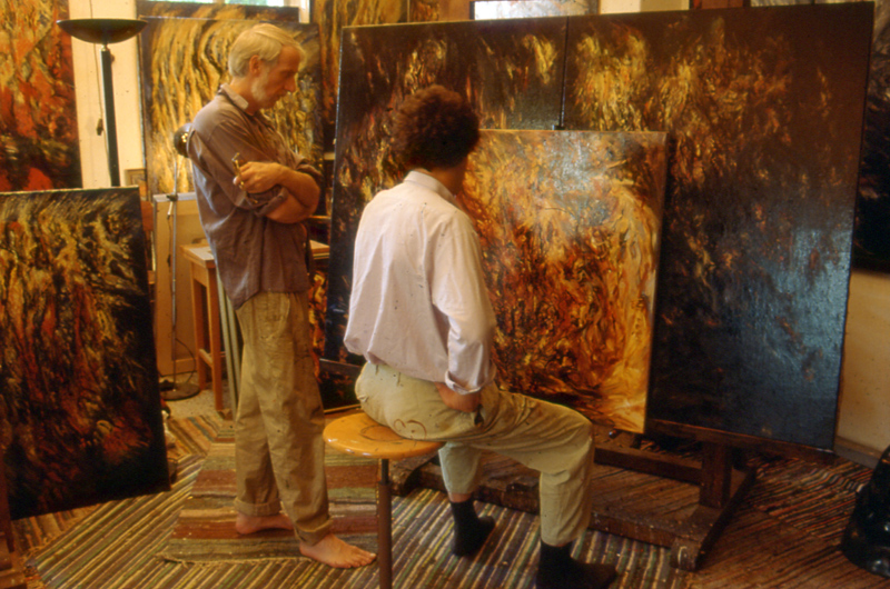 Hans Praetterhoffer painting a large canvas with a visitor nearby