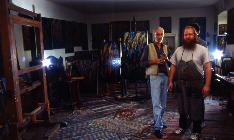 Two people standing among paintings in the studio