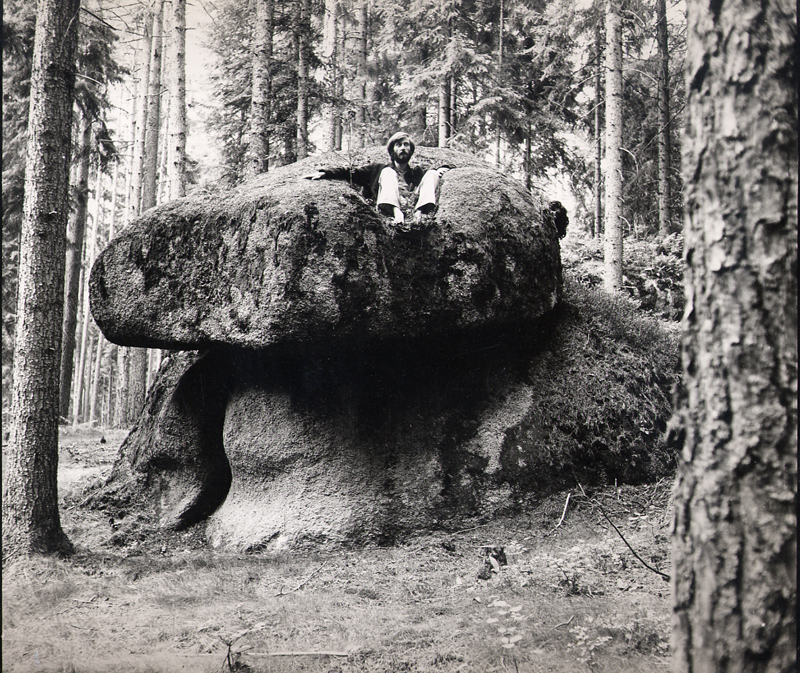 Figure standing beneath a large boulder in a forest